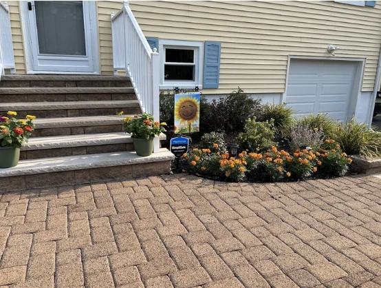 Front entrance of a home featuring landscaped garden beds with vibrant marigolds and greenery, flanked by potted flowers on stone steps, showcasing sustainable landscaping design by Gebhard Horticulture & Design.