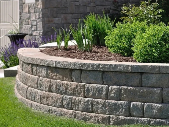 Curved stone garden bed featuring lush green plants and vibrant lavender, illustrating professional garden bed design and sustainable landscaping services.
