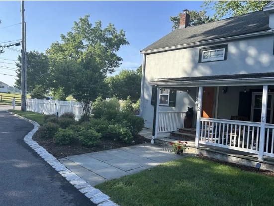 House exterior with well-maintained garden beds, featuring a stone walkway, lush greenery, and a welcoming porch, emphasizing sustainable landscaping and garden design.