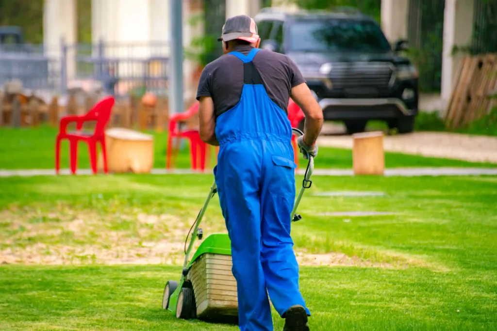 gardener worker cutting grass with mower in the yard