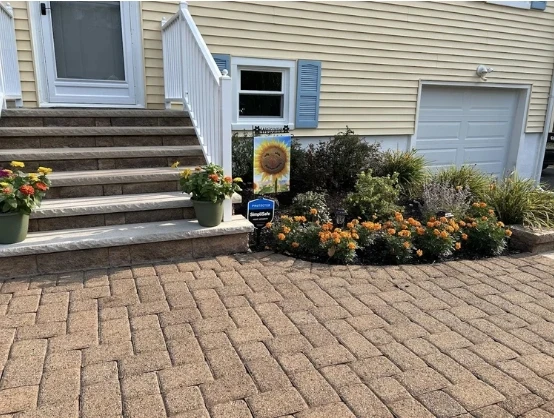 Front entrance of a home featuring landscaped garden beds with vibrant marigolds and greenery, flanked by potted flowers on stone steps, showcasing sustainable landscaping design by Gebhard Horticulture & Design.