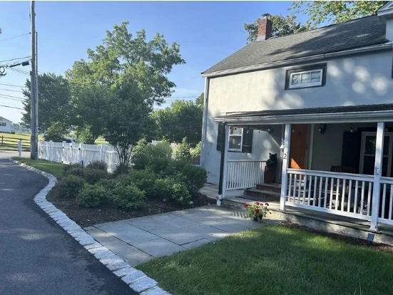 House exterior with well-maintained garden beds, featuring a stone walkway, lush greenery, and a welcoming porch, emphasizing sustainable landscaping and garden design.